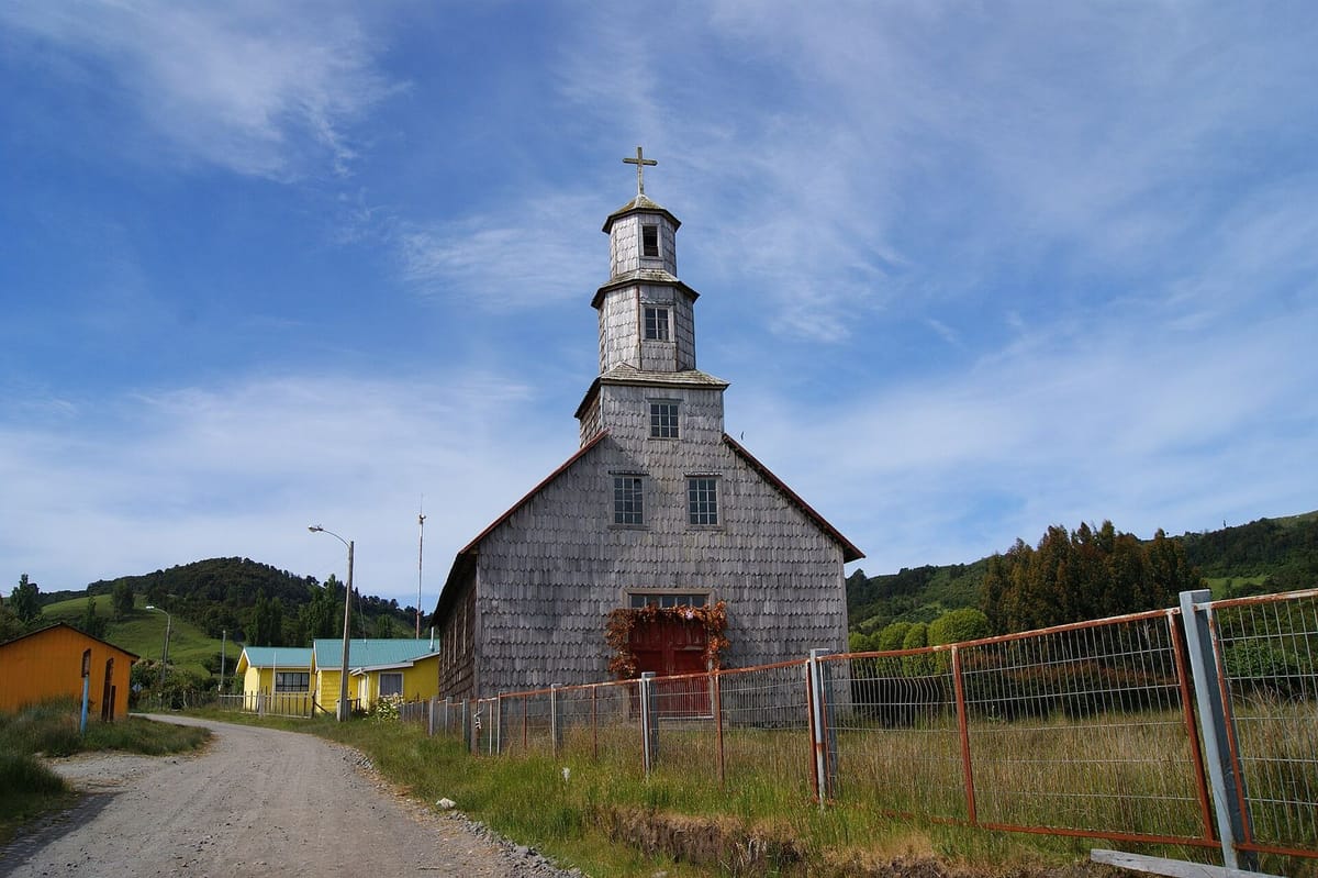 Gereja kayu bercat khas Chiloé dengan menara di depan lapangan