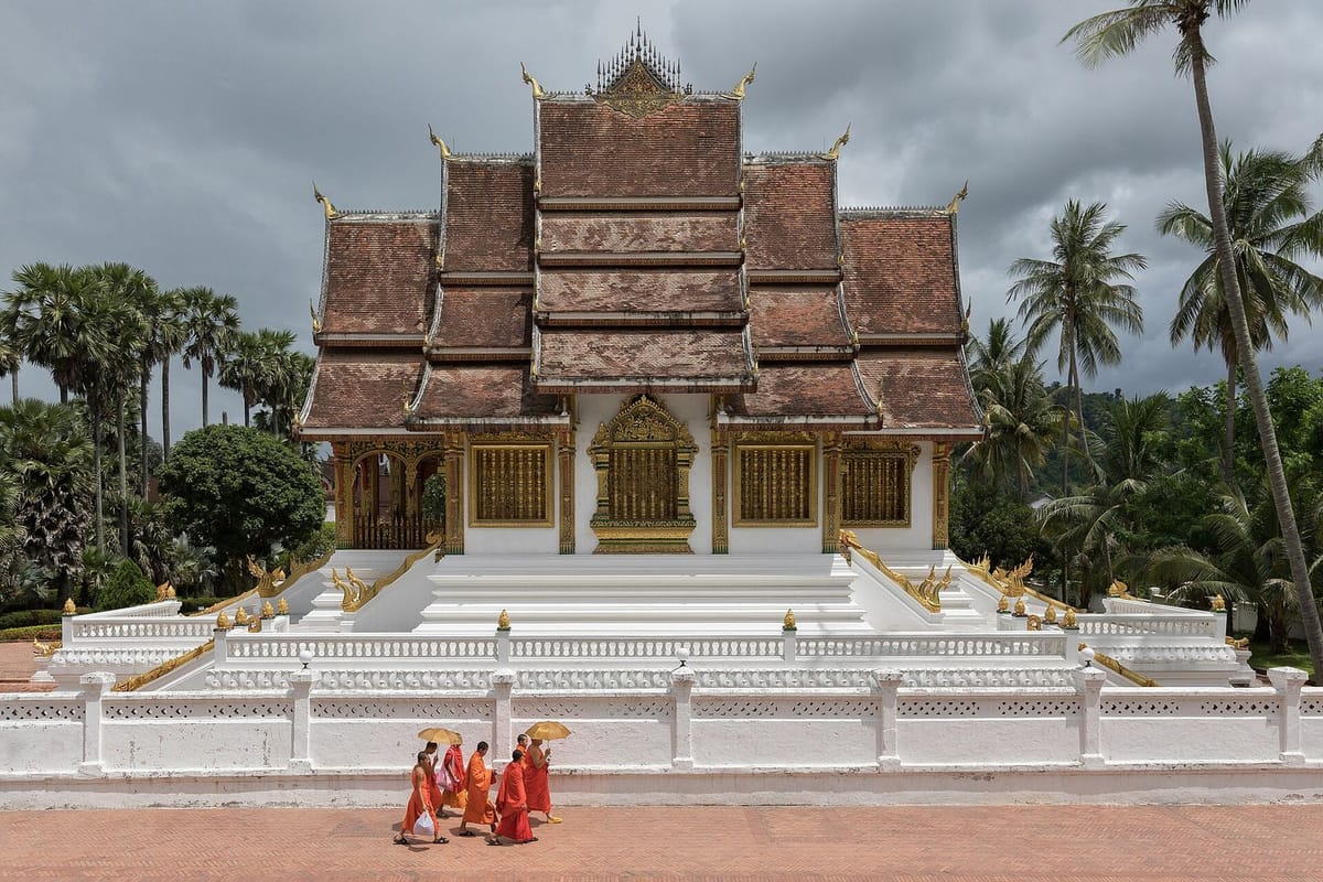 Biksu berjalan di depan kuil Haw Pha Bang, Luang Prabang
