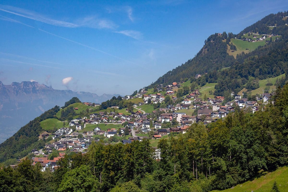 Desa di lereng gunung dengan gereja dan pegunungan Alpen di belakangnya